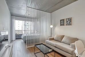 Una sala moderna con una mesa de centro de vidrio, un sofá color beige y un separador blanco.