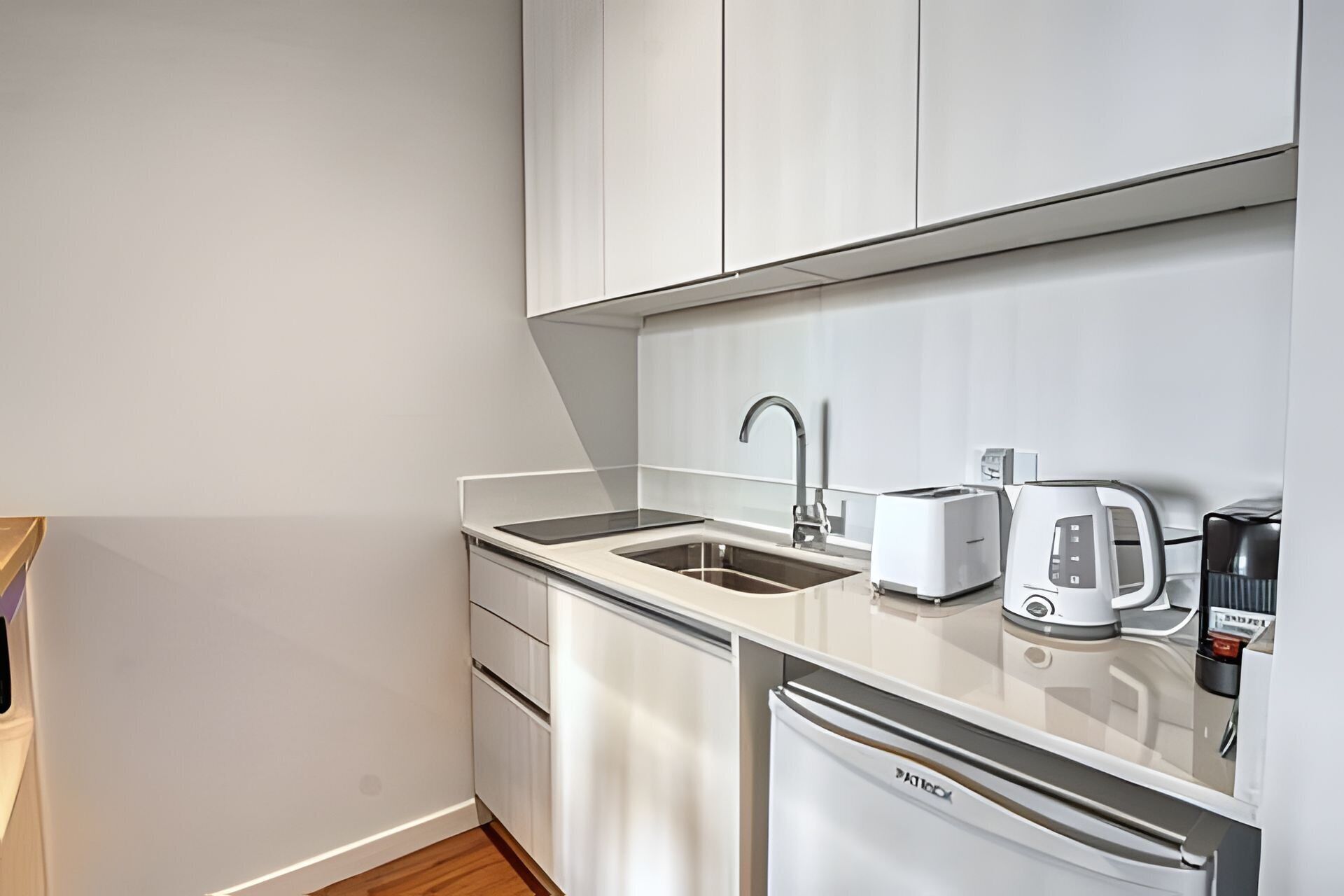 A compact kitchenette with a sink, a toaster, a kettle, and a refrigerator.