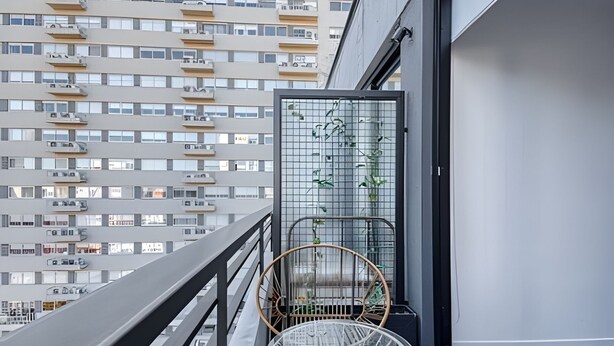 Un balcone con una sedia e un'ampia vetrata, affacciato su un palazzo con numerosi balconi.