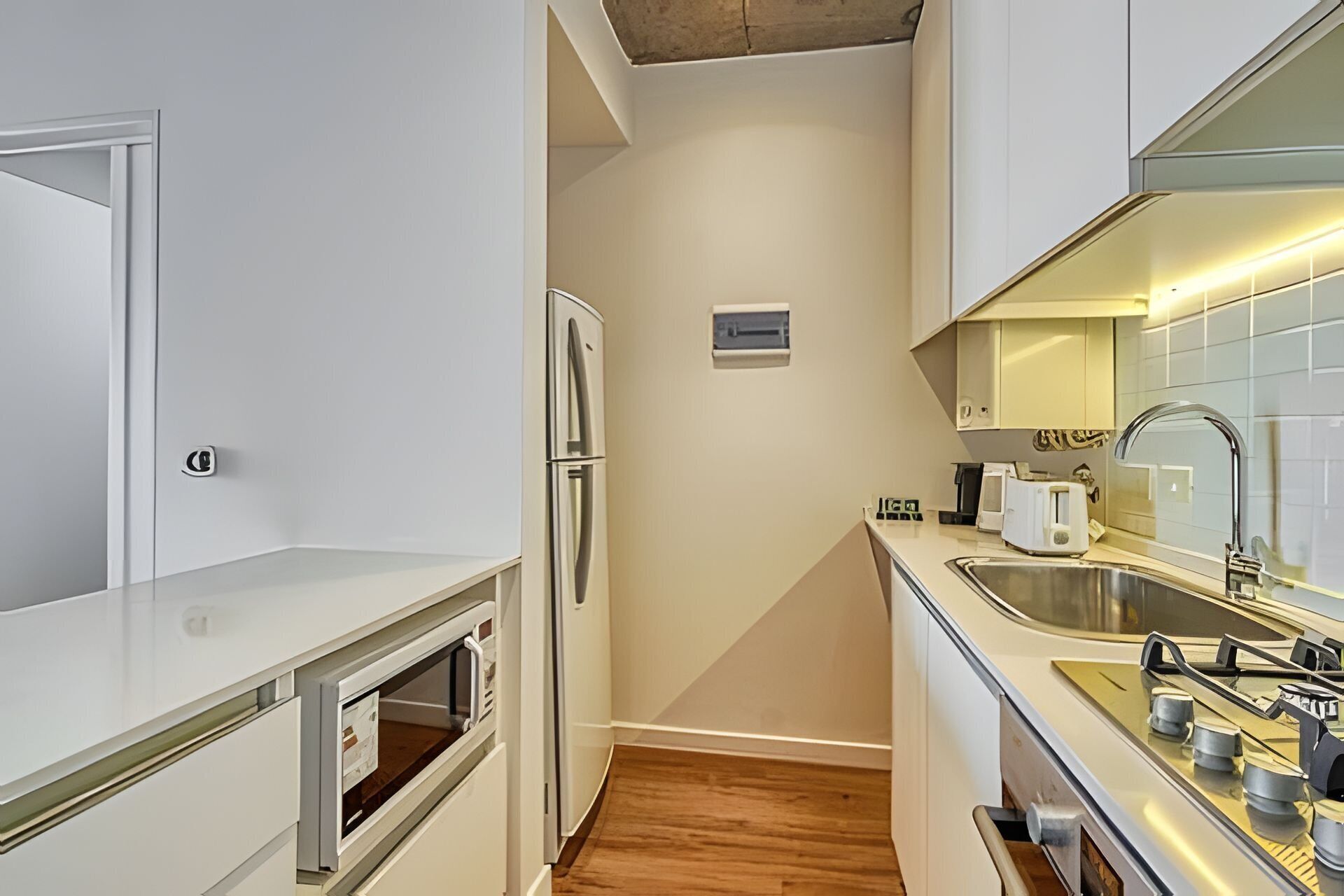 A compact kitchen with white cabinets, a built-in oven, a refrigerator, a sink, and a toaster.