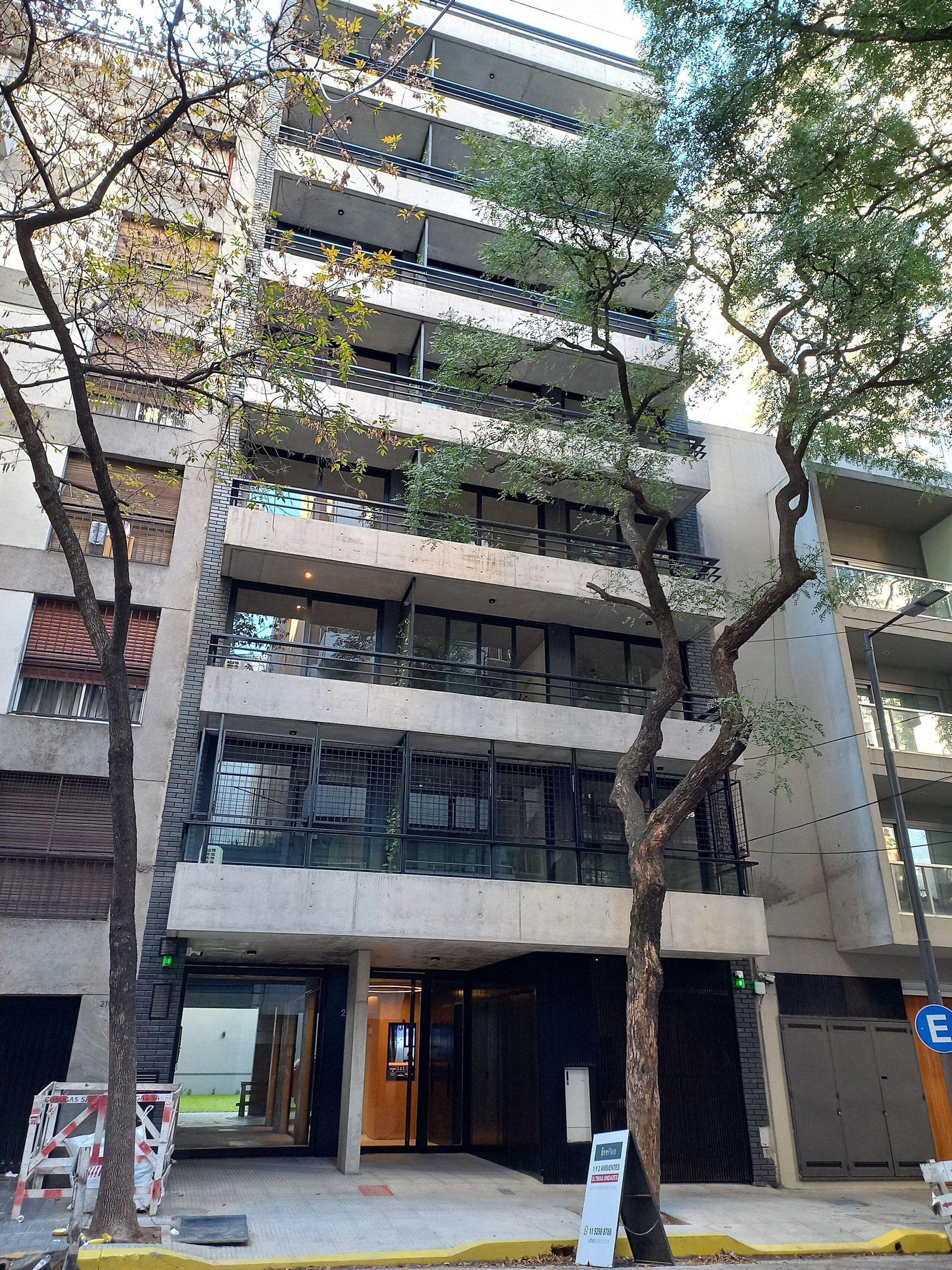 Un edificio de varios pisos con un diseño arquitectónico moderno, que cuenta con balcones, ventanas amplias y una entrada a nivel de calle.