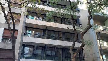 Un edificio de varios pisos con un diseño arquitectónico moderno, que cuenta con balcones, ventanas amplias y una entrada a nivel de calle.