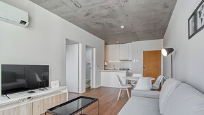 Ett modernt vardagsrum med en platt-TV, ett soffbord i glas, en soffa och en matplats med stolar.