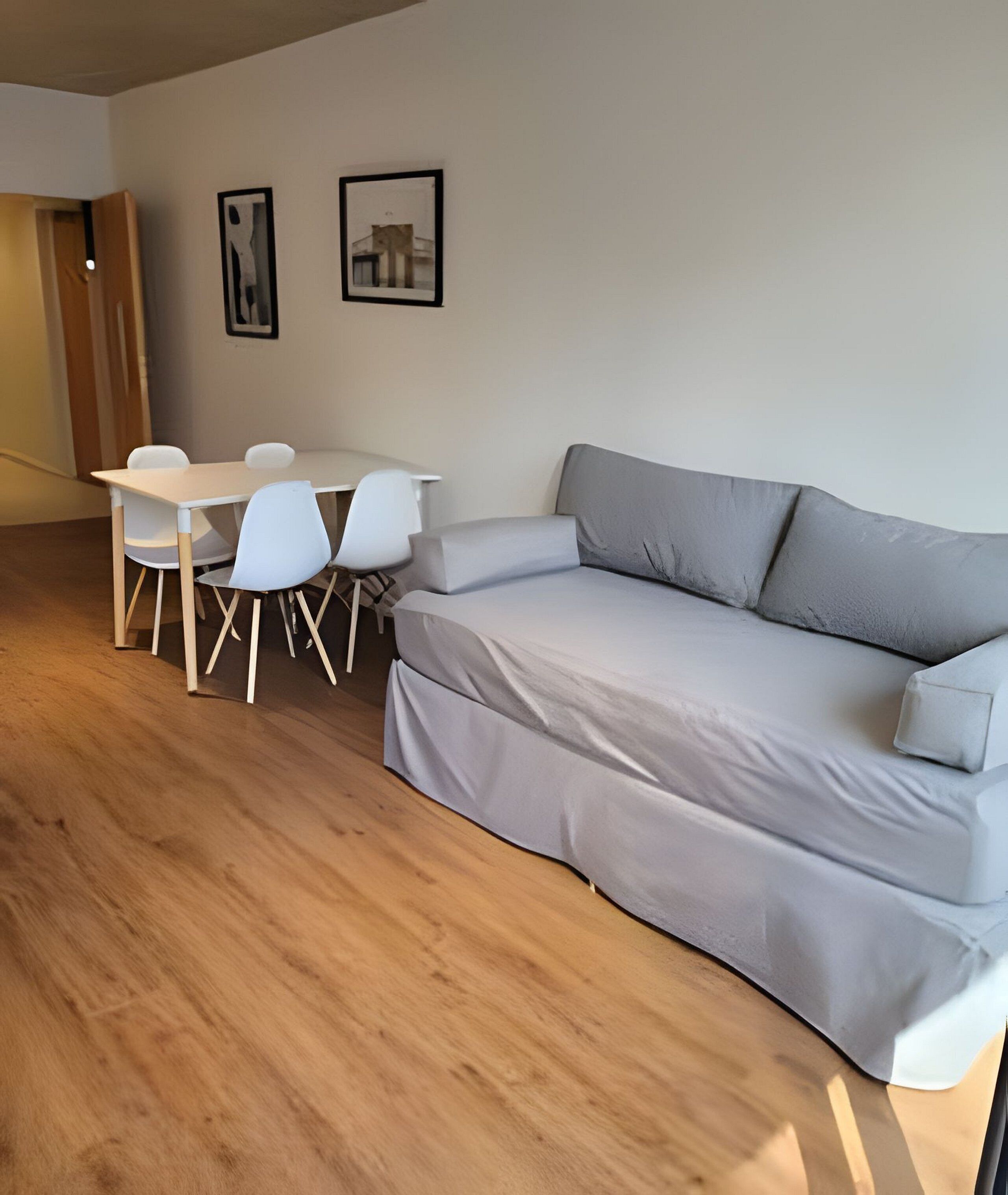 Ett modernt vardagsrum med en grå soffa, vita stolar, ett litet bord och två inramade tavlor på väggen.