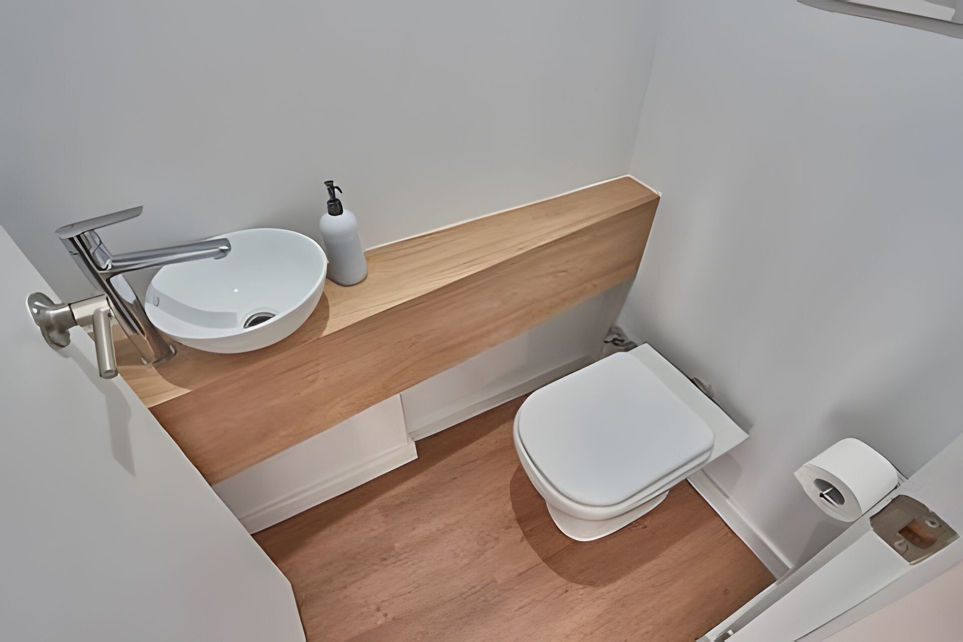 Um banheiro pequeno e moderno com pia branca, vaso sanitário e toucador de madeira.