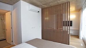 A modern bedroom with a large bed, a wooden slat partition, a mounted TV, and a built-in air conditioning unit. - Your Temporary Home in the City: Comfortable and Central Apartment (Ciudad Autónoma de Buenos Aires)