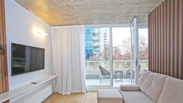 A modern living room with a flat-screen TV, a beige sofa, and a sliding glass door leading to an outdoor balcony. - Your Temporary Home in the City: Comfortable and Central Apartment (Ciudad Autónoma de Buenos Aires)