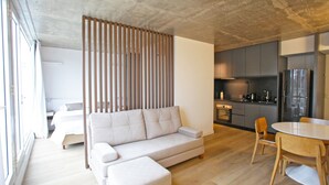 A modern living room with a sofa, a dining table with chairs, a kitchen area, and a large window providing natural light. - Your Temporary Home in the City: Comfortable and Central Apartment (Ciudad Autónoma de Buenos Aires)