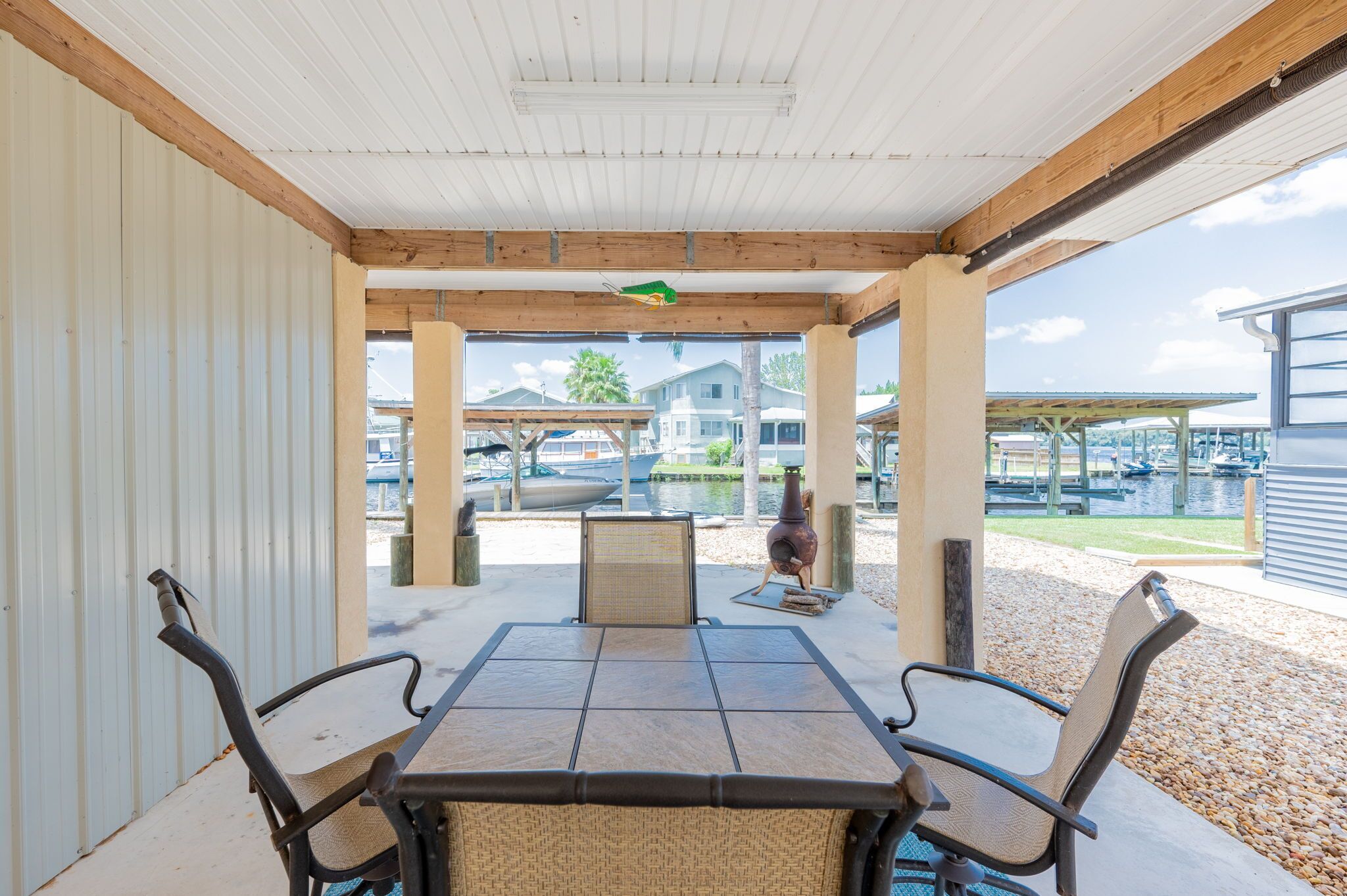 A covered patio with a table and chairs, overlooking a marina with boats and houses.