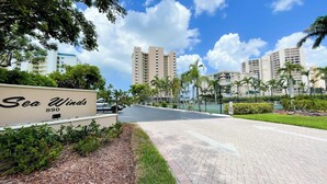 A paved pathway leading to a building labeled "Sea Winds 890" with a clear sky and tall buildings in the background. - Sea Winds 1401: Beach Front; Pool View (Marco Island)
