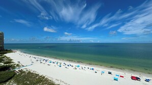 A beach with white sand, clear blue water, and a few umbrellas. - Sea Winds 1401: Beach Front; Pool View (Marco Island)