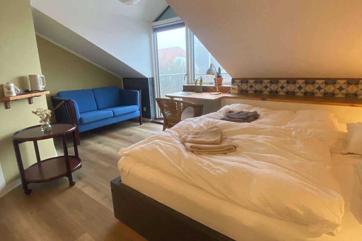 Ein Schlafzimmer mit einem Bett, einem Schreibtisch, einem Stuhl, einem blauen Sofa und einem kleinen Tisch mit einer Lampe.