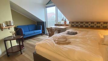 A bedroom with a bed, a desk, a chair, a blue sofa, and a small table with a lamp.