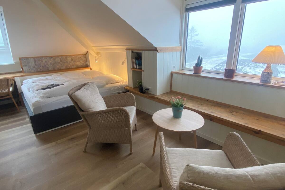 Ein gemütliches Schlafzimmer mit einem Bett, zwei Stühlen, einem kleinen Tisch und einem Fenster mit Aussicht.
