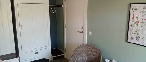 A room with a white wardrobe, a wicker chair, a radiator, and a framed botanical print on the wall.