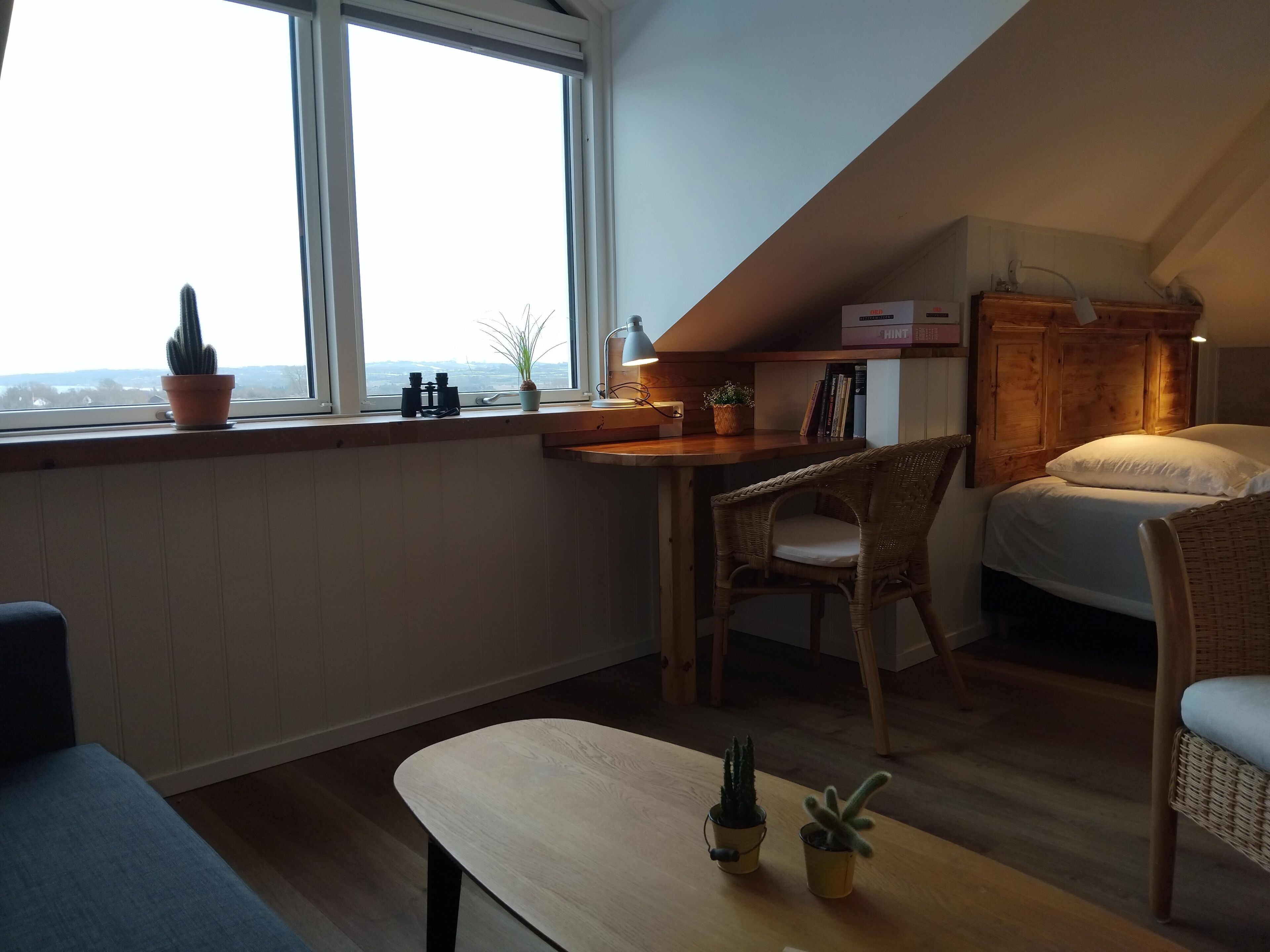 A cozy room with a bed, a desk with a lamp, a chair, and a view through a window.