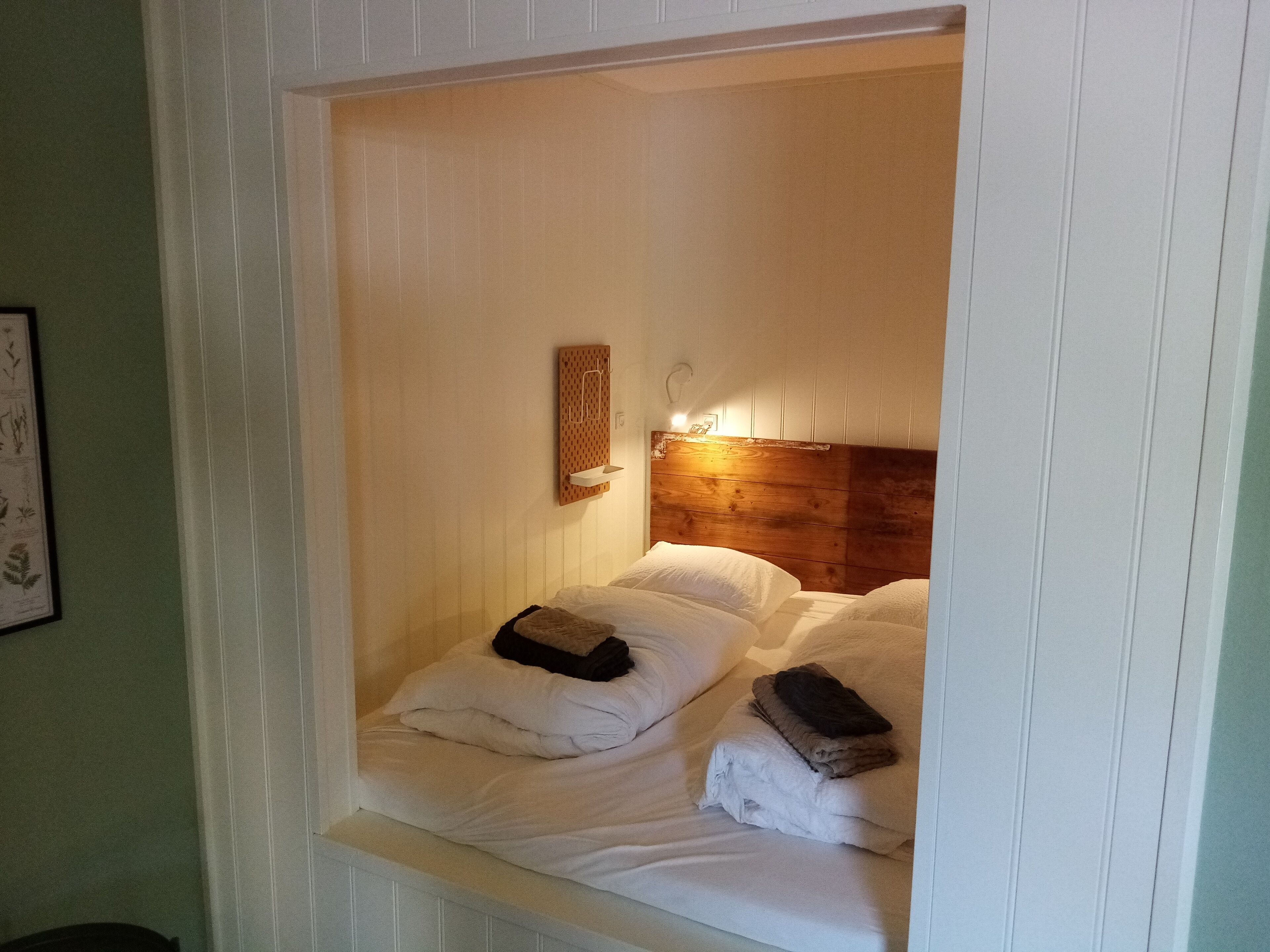 Um quarto pequeno e acolhedor, com cabeceira de madeira, mesa de cabeceira com luminária e camas bem arrumadas.
