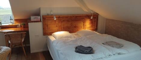 Una camera da letto con una testiera in legno, una scrivania con una lampada, una sedia in vimini e un letto con biancheria da letto bianca.
