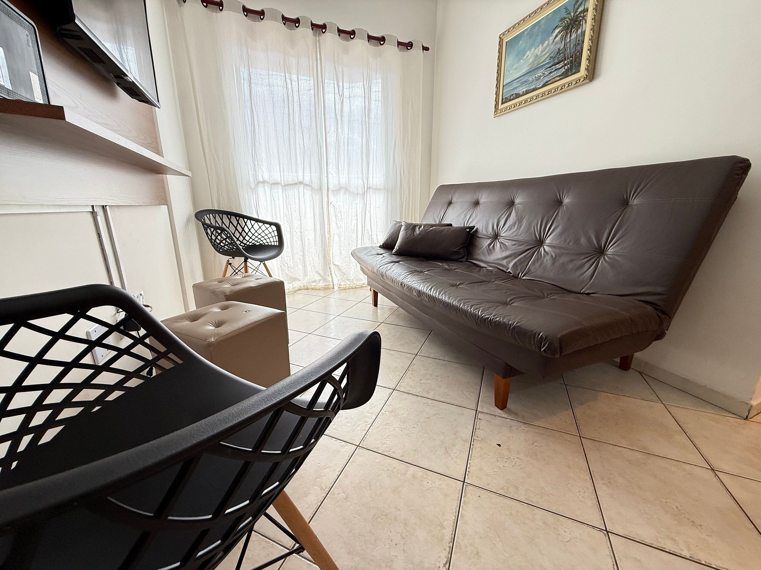Uma sala de estar com um sofá, uma poltrona, uma mesinha e um quadro na parede.