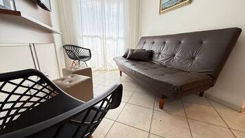 Uma sala de estar com um sofá, uma poltrona, uma mesinha e um quadro na parede.