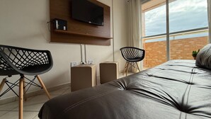 Camera da letto moderna con un letto grande, una TV a parete, due poltrone e vista sul cielo attraverso un'ampia finestra.