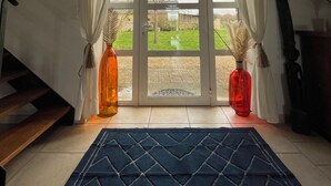 Ein Zimmer mit einer großen Glastür, die zu einem Garten führt, einem dunkelblauen Teppich und zwei Vasen auf dem Boden.