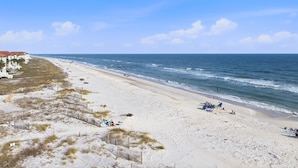 A beach with a sandy shore, a few beachgoers, and a row of white buildings with red roofs. - Ocean Mile I-4 - Beach Front, Swimming Pool, Beach Gear Included! (St George Island)