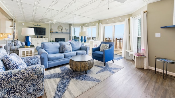 A spacious living room with a blue sofa, a round coffee table, and a ceiling fan. - Ocean Mile I-4 - Beach Front, Swimming Pool, Beach Gear Included! (St George Island)