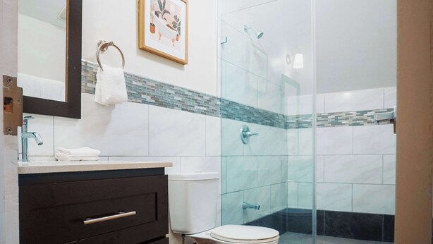 Une salle de bain moderne avec une douche à parois de verre, des toilettes blanches, un meuble-lavabo avec un miroir et un tableau encadré au mur.