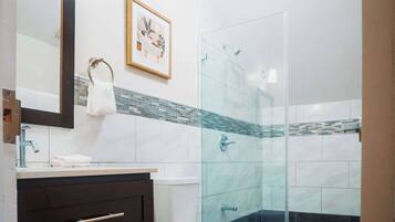 A modern bathroom with a glass shower enclosure, a white toilet, a vanity with a mirror, and a framed picture on the wall.
