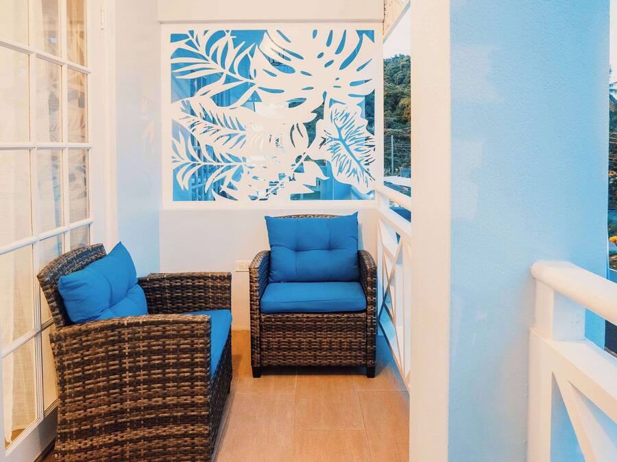 A balcony with wicker furniture and blue cushions, a decorative leaf pattern on the wall, and a view of the outdoors.