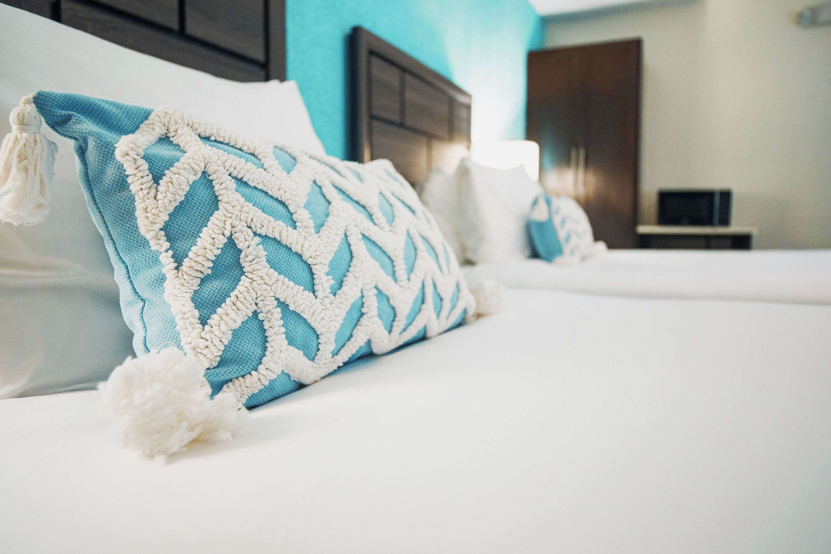 Uma cama bem arrumada com uma almofada estampada em azul e branco, uma almofada fofa branca e uma almofada branca.