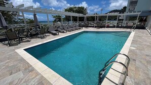 Una piscina rectangular con agua cristalina, rodeada de sillas de descanso y sombrillas, y una estructura de pérgola.
