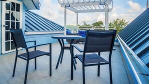 Una terraza en la azotea con dos sillas y una mesa, un pérgola y vistas al cielo y al paisaje lejano.