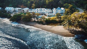 Un hôtel situé sur la côte, composé de plusieurs bâtiments, avec une plage et une colline boisée.