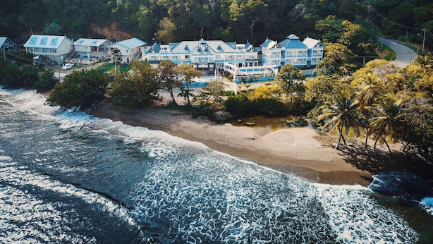 Un hotel en la costa con varias edificaciones, una playa y un promontorio cubierto de bosque.