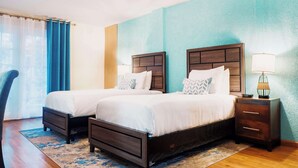 Habitación de hotel con dos camas, piso de madera, pared decorativa azul, una lámpara de techo y una mesita de noche con lámpara.
