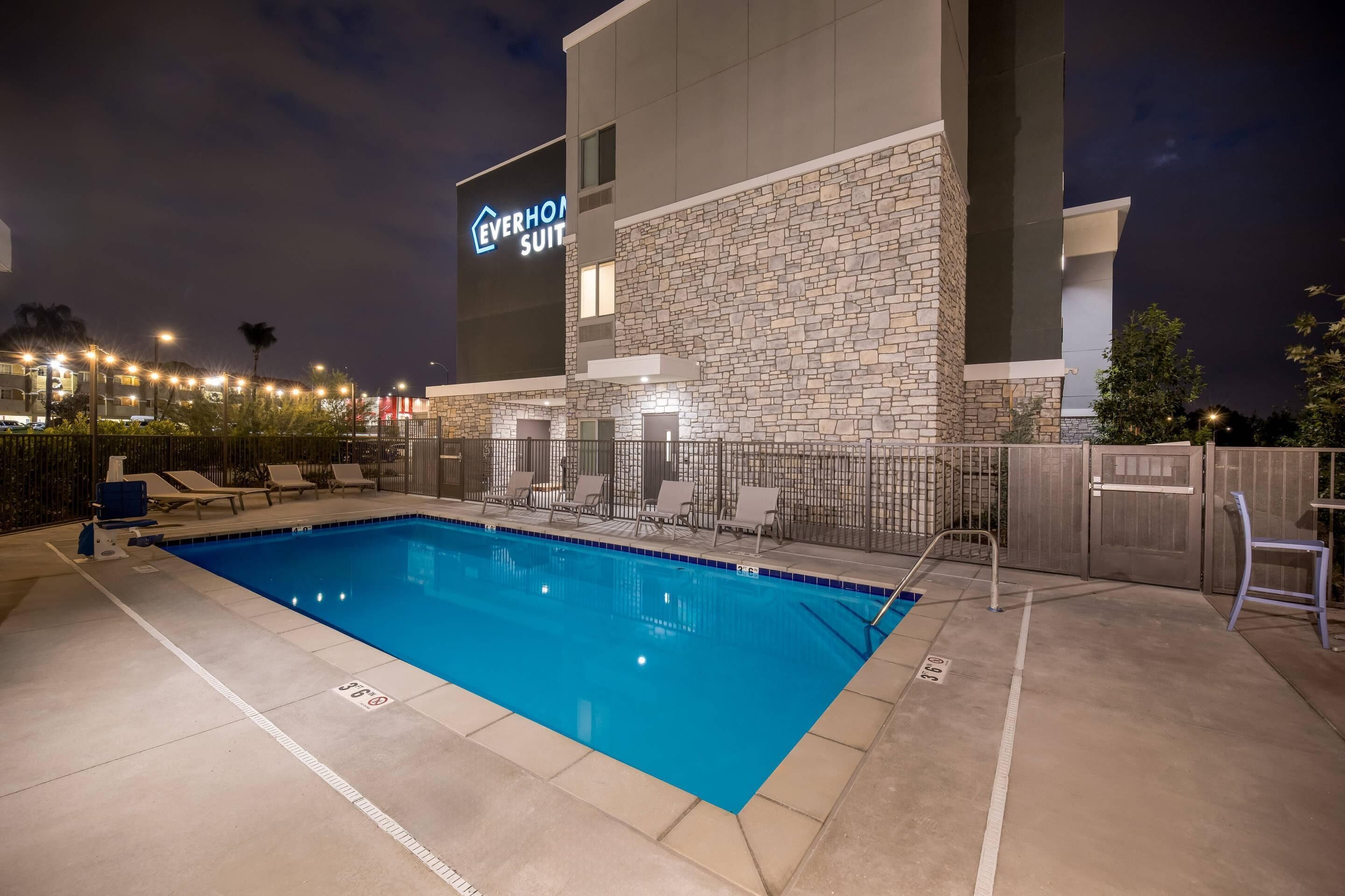 A hotel pool area with a stone facade, lounge chairs, and a sign for 'Everhome Suites'.