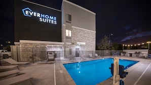Moderni hotellin ulkoasu, jossa on uima-allas, ulkotila istumiseen ja suuri kyltti, jossa lukee ”Everhome Suites”.