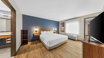 A modern hotel room with a large bed, wooden flooring, a built-in wardrobe, bedside lamps, and a large window.