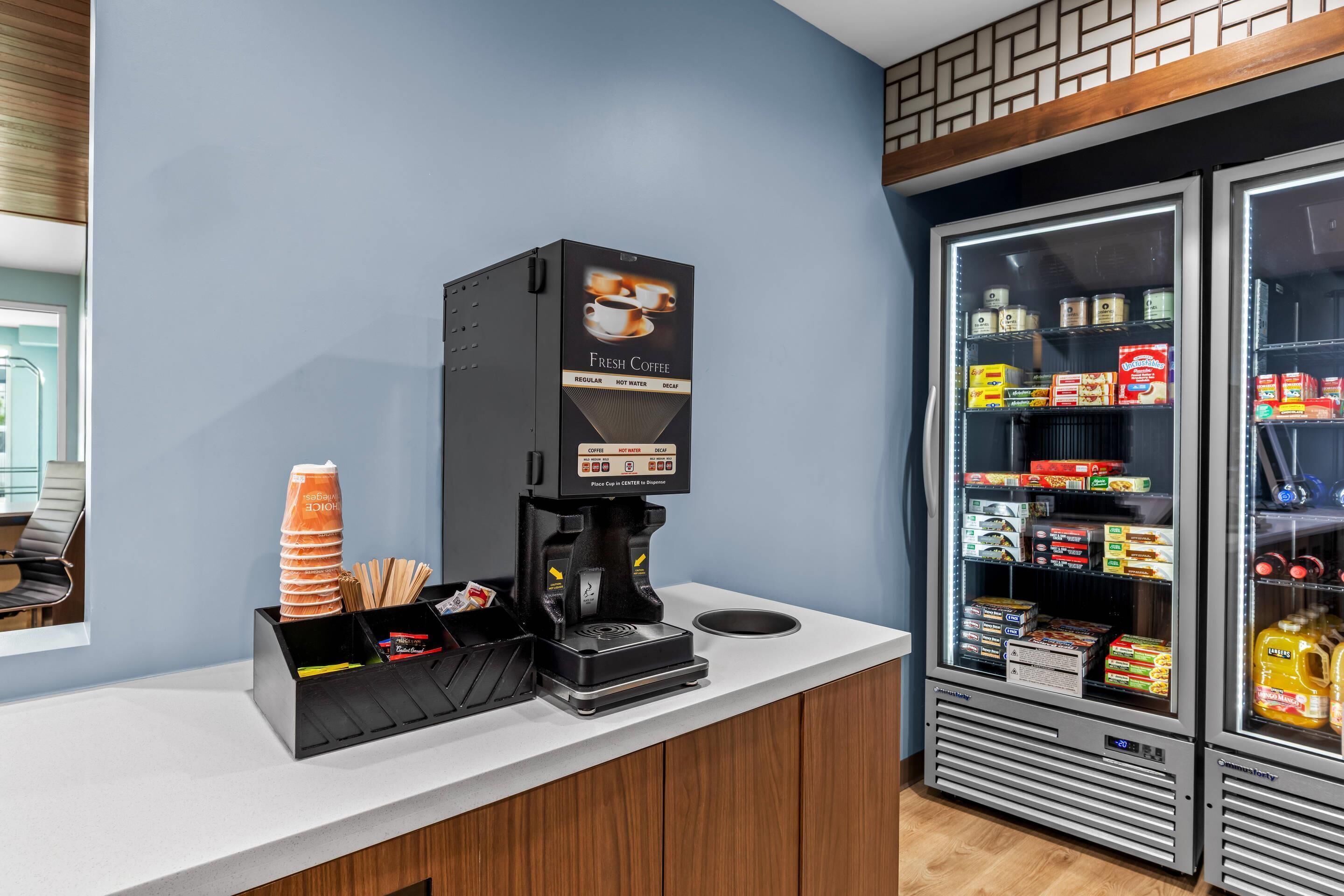 Una cafetera con una vitrina para tazas de café y un refrigerador lleno de bebidas y aperitivos.