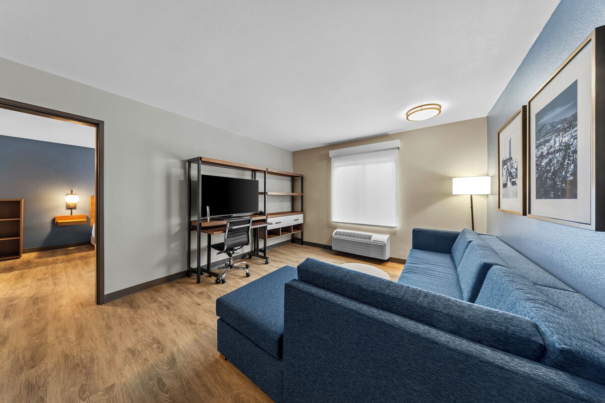 Una sala de estar moderna con un sofá, un escritorio con una computadora, un televisor y una ventana con persianas.