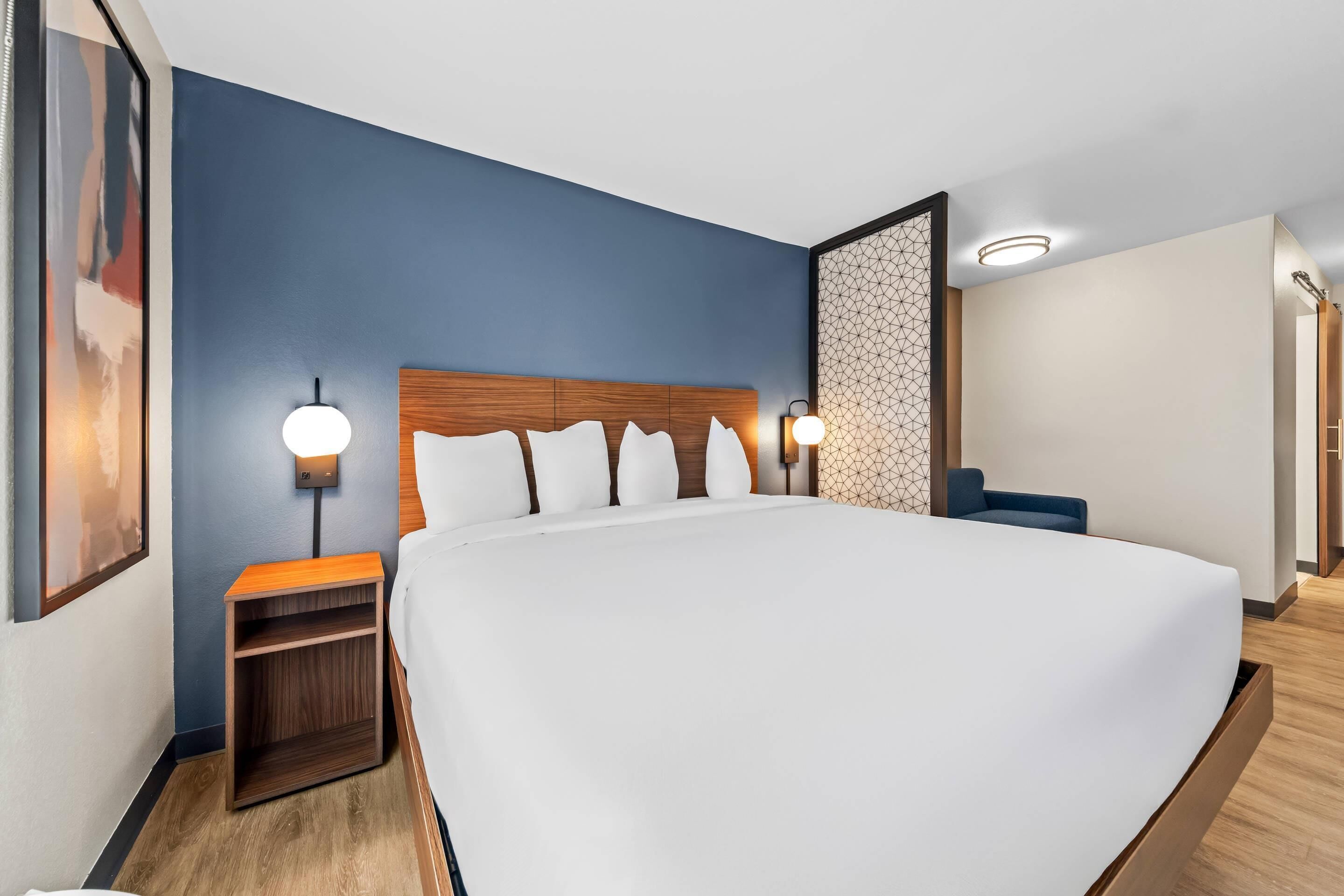 A modern hotel room with a large bed, wooden headboard, two bedside tables with lamps, and a geometric-patterned wall.