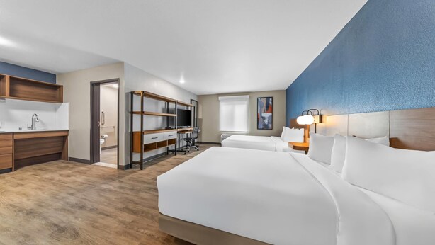 Hotellihuone, jossa on suuri sänky, työpöytä tuolilla, kylpyhuone ja pieni keittiönurkkaus.