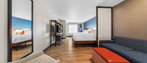 Una habitación de hotel con una cama grande, un escritorio con una silla, un sofá y un pequeño otoman.