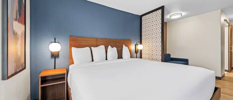 Een moderne hotelkamer met een groot bed, een houten hoofdbord, twee nachtkastjes met lampen en een scheidingswand met een geometrisch patroon.