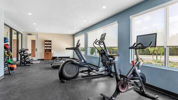 Un gimnasio con equipo de ejercicio, ventanas amplias y vistas al exterior.
