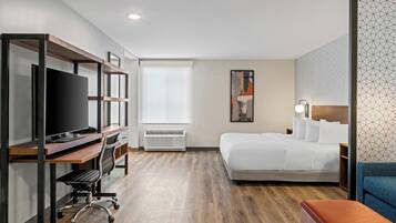 A hotel room with a bed, a desk with a TV, a chair, a heater, and a window.