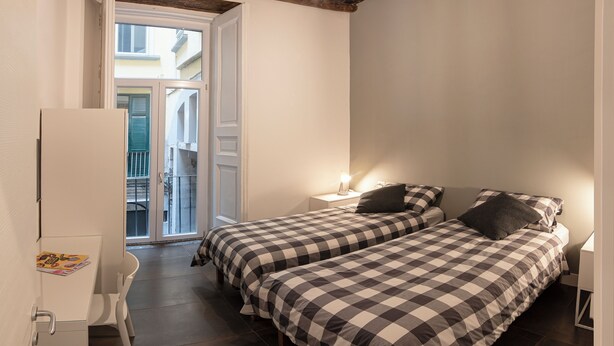 Une petite chambre bien éclairée, avec deux lits, un bureau et une chaise.
