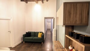 Un couloir étroit avec un canapé vert, un banc en bois et une porte blanche.